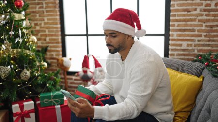 Foto de Hombre afroamericano usando smartphone sosteniendo regalo de Navidad en casa - Imagen libre de derechos