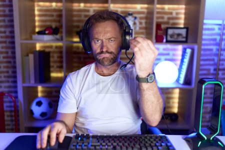 Téléchargez les photos : Moyen Age homme avec barbe jouer à des jeux vidéo portant un casque faire geste italien avec la main et les doigts expression confiante - en image libre de droit