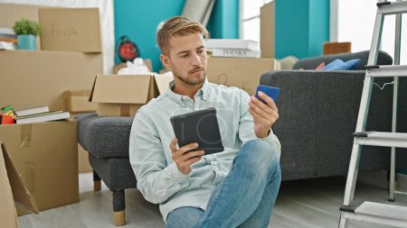 Téléchargez les photos : Jeune homme caucasien faisant du shopping avec touchpad et carte de crédit assis sur le sol à la nouvelle maison - en image libre de droit