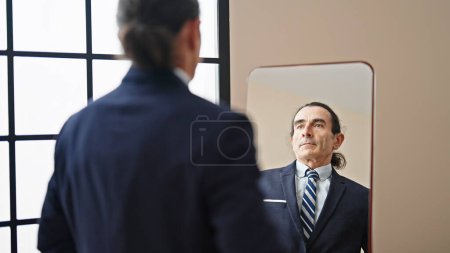 Foto de Hombre de mediana edad trabajador de negocios mirando en el espejo con cara seria en casa - Imagen libre de derechos