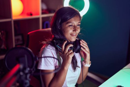 Photo for Young beautiful hispanic woman streamer smiling confident holding headphones at gaming room - Royalty Free Image