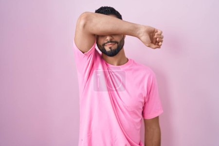 Photo for Hispanic young man standing over pink background covering eyes with arm, looking serious and sad. sightless, hiding and rejection concept - Royalty Free Image