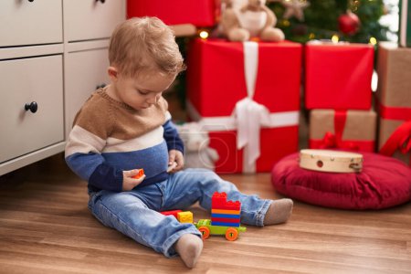 Téléchargez les photos : Adorable tout-petit jouant avec des blocs de construction assis sur le sol par des cadeaux de Noël à la maison - en image libre de droit
