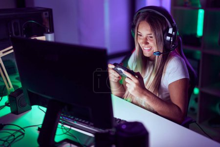 Foto de Young beautiful hispanic woman streamer playing video game using smartphone at gaming room - Imagen libre de derechos