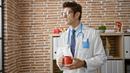 Téléchargez les photos : Jeune homme hispanique médecin tenant une tasse de café à la clinique - en image libre de droit