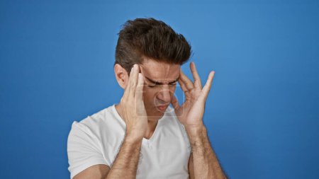 Foto de Hombre hispano joven que sufre de dolor de cabeza sobre un fondo azul aislado - Imagen libre de derechos
