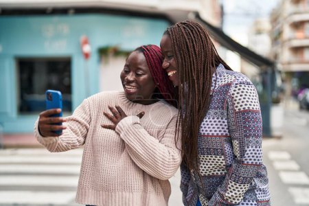 Foto de Afro-americanas amigas sonriendo confiadas teniendo videollamada en la calle - Imagen libre de derechos