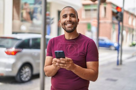 Photo for Young latin man smiling confident using smartphone at street - Royalty Free Image