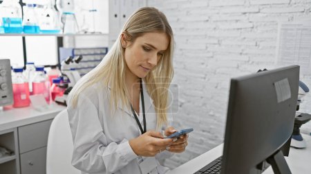 Téléchargez les photos : Jolie jeune femme blonde scientifique concentrée sur son smartphone au laboratoire, un beau portrait au milieu de la recherche et de l'analyse médicales - en image libre de droit