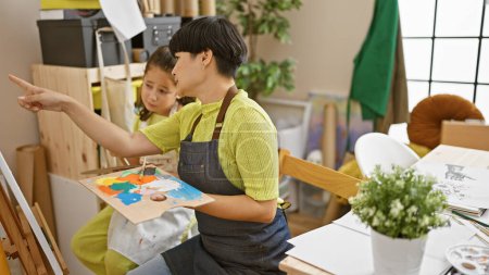 Téléchargez les photos : Enseignant et étudiant artiste se lient alors qu'ils se réunissent en classe d'art dans un atelier intérieur, apprennent à peindre des toiles et parlent de techniques de pinceaux - en image libre de droit