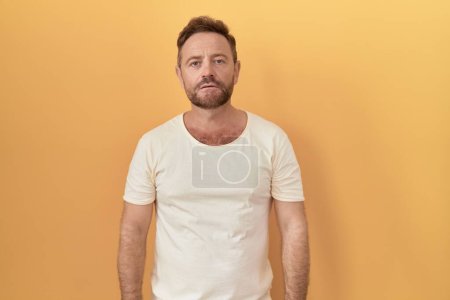 Photo for Middle age man with beard standing over yellow background relaxed with serious expression on face. simple and natural looking at the camera. - Royalty Free Image