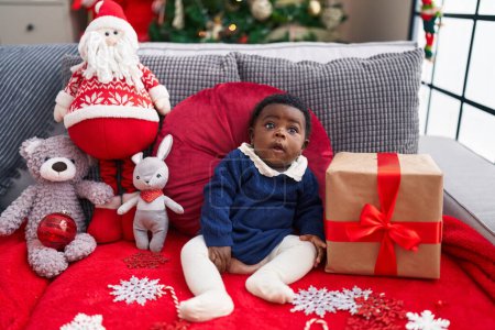 Foto de Bebé afroamericano sentado en el sofá por el árbol de Navidad en casa - Imagen libre de derechos