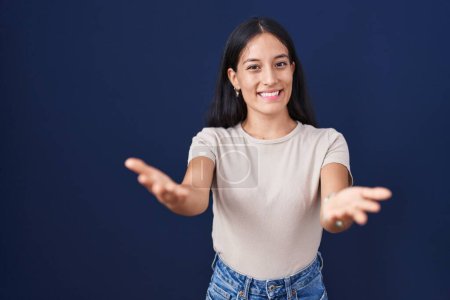 Téléchargez les photos : Jeune femme hispanique debout sur fond bleu souriant joyeuse offrant des mains donnant assistance et acceptation. - en image libre de droit