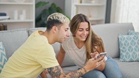Téléchargez les photos : Beau couple utilisant smartphone souriant à la maison - en image libre de droit
