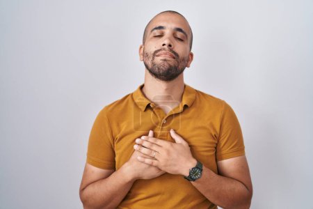 Photo for Hispanic man with beard standing over white background smiling with hands on chest with closed eyes and grateful gesture on face. health concept. - Royalty Free Image