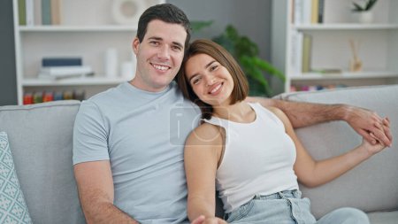 Photo for Beautiful couple sitting on sofa hugging each other smiling at home - Royalty Free Image