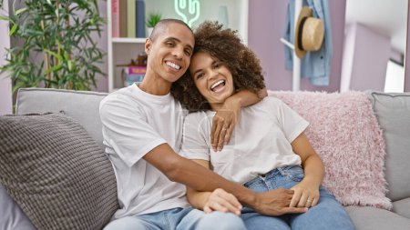 Photo for Beautiful couple sitting on sofa, hugging with radiant smiles in their cozy home. a testament of love, an expression of joy and confidence reigns in the room as their casual lifestyle shines through. - Royalty Free Image
