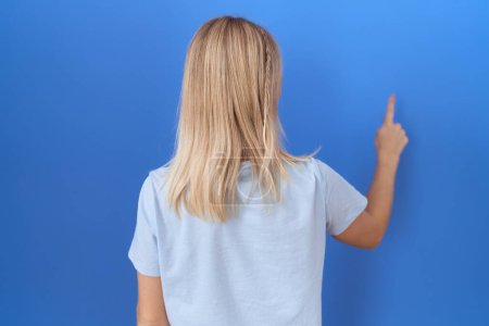Photo for Young caucasian woman wearing casual blue t shirt posing backwards pointing ahead with finger hand - Royalty Free Image