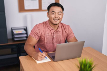 Photo for Young chinese man business worker using laptop writing on notebook at office - Royalty Free Image