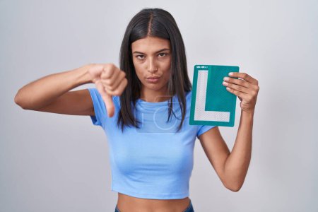 Photo for Brunette young woman holding l sign for new driver with angry face, negative sign showing dislike with thumbs down, rejection concept - Royalty Free Image
