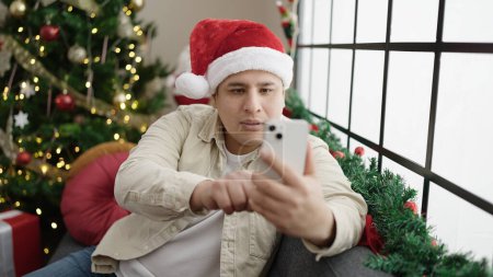 Photo for Young hispanic man make selfie by smartphone celebrating christmas at home - Royalty Free Image