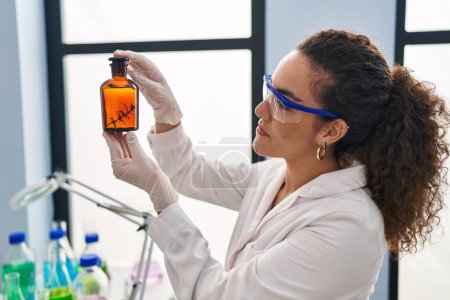 Foto de Joven hermosa mujer hispana científica sosteniendo tubo de ensayo con planta en laboratorio - Imagen libre de derechos