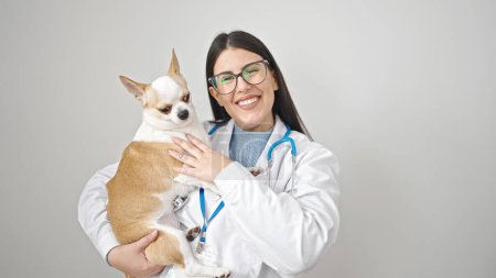 Foto de Joven mujer hispana con perro veterinario chihuahua sonriendo sosteniendo perro sobre fondo blanco aislado - Imagen libre de derechos