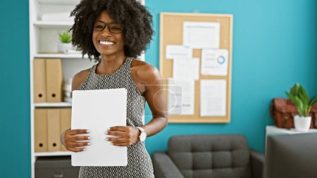 Téléchargez les photos : Femme afro-américaine d'affaires détenant des documents souriant au bureau - en image libre de droit