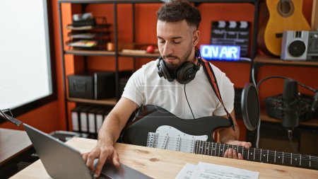 Photo for Young arab man musician playing electrical guitar composing song using laptop at music studio - Royalty Free Image