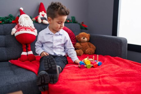 Photo for Adorable hispanic toddler playing with train toy sitting on sofa by christmas decoration at home - Royalty Free Image