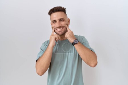 Téléchargez les photos : Hispanic man with beard standing over white background smiling with open mouth, fingers pointing and forcing cheerful smile - en image libre de droit