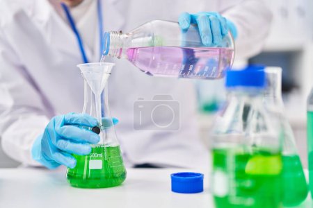 Téléchargez les photos : Young caucasian man scientist pouring liquid on test tube at laboratory - en image libre de droit