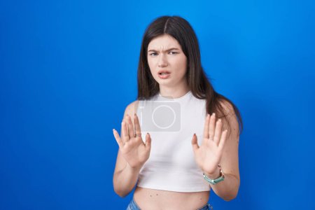 Photo for Young caucasian woman standing over blue background moving away hands palms showing refusal and denial with afraid and disgusting expression. stop and forbidden. - Royalty Free Image