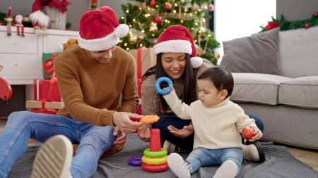 Foto de Pareja e hijo sentados en el suelo por árbol de Navidad jugando con aros de juguete en casa - Imagen libre de derechos