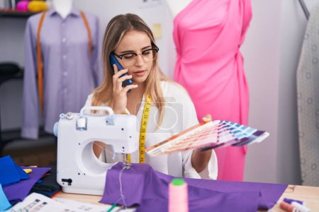 Téléchargez les photos : Young blonde woman tailor talking on smartphone choosing color at clothing shop - en image libre de droit