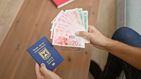 Téléchargez les photos : Jeune homme comptant les billets de banque en shekels sur le canapé à la maison, un aperçu de la vie adulte d'un détenteur de passeport israélien - en image libre de droit