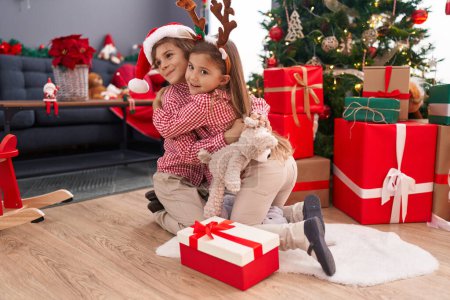 Foto de Hermano y hermana abrazándose el uno al otro sentados en el suelo por el árbol de Navidad en casa - Imagen libre de derechos