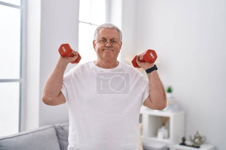Foto de Hombre de pelo gris de mediana edad sonriendo confiado usando pesas de entrenamiento en casa - Imagen libre de derechos