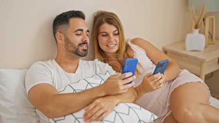 Téléchargez les photos : Homme et femme couple assis sur le lit à l'aide de smartphones parlant dans la chambre - en image libre de droit