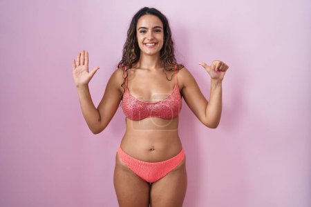 Téléchargez les photos : Jeune femme hispanique portant de la lingerie sur fond rose montrant et pointant vers le haut avec les doigts numéro six tout en souriant confiant et heureux. - en image libre de droit