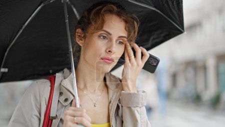 Téléchargez les photos : Jeune femme écoutant un message vocal tenant un parapluie dans la rue - en image libre de droit
