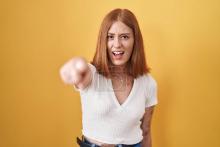 Photo for Young redhead woman standing over yellow background pointing displeased and frustrated to the camera, angry and furious with you - Royalty Free Image