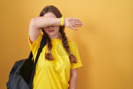 Photo for Young caucasian woman wearing student backpack over yellow background covering eyes with arm, looking serious and sad. sightless, hiding and rejection concept - Royalty Free Image