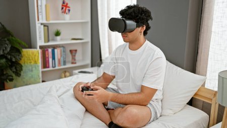 Foto de Joven latino jugando videojuegos con gafas de realidad virtual y joystick en el dormitorio - Imagen libre de derechos