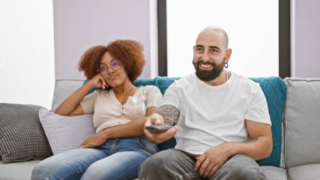 Photo for Joyful and beautiful couple enjoying fun time together at home sitting comfortably on their living room sofa, laughing and confidently changing channels, watching their favorite movie on television - Royalty Free Image
