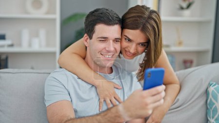 Foto de Hermosa pareja abrazándose usando el teléfono inteligente sonriendo en casa - Imagen libre de derechos