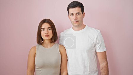 Foto de Hermosa pareja de pie junto con cara seria sobre fondo rosa aislado - Imagen libre de derechos