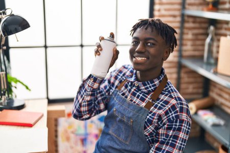 Téléchargez les photos : Africain américain artiste souriant confiant tenant pulvérisation de graffiti au studio d'art - en image libre de droit