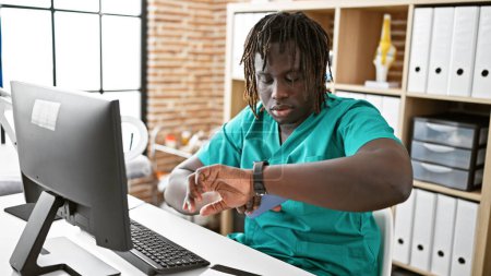 Téléchargez les photos : Afro-Américain homme médecin en utilisant ordinateur regarder avec sérieux visage à la clinique - en image libre de droit