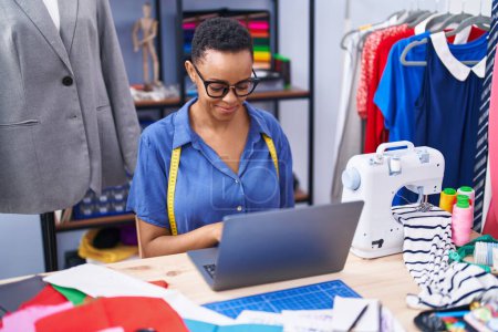 Téléchargez les photos : Femme afro-américaine tailleur souriant confiant en utilisant un ordinateur portable au magasin de tailleur - en image libre de droit